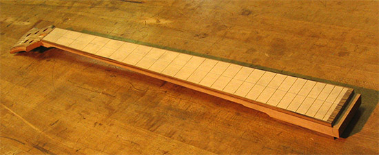 Maple fretboard and zebra wood binding on a five string bass neck
