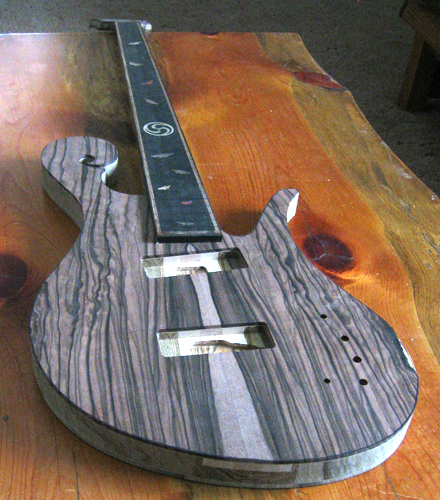 Front of the 5 string custom bass from a low angle. Macassar ebony, black limba core wood and ebony fretboard are pictured.