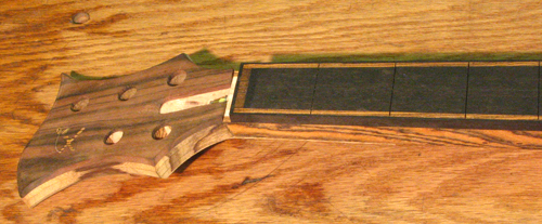 The custom bass neck from the side showing the ebony binding around the bocote accented fretboard, the black limba headstock core and the macassar ebony headstock veneer