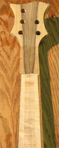 Back of the custom bass guitar's headstock with tuner holes and bookmatched black limba veneer