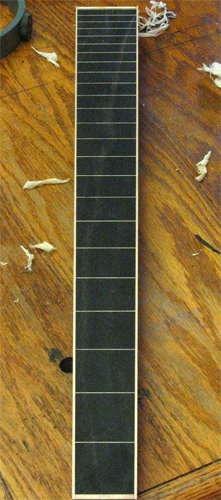 The maple bound ebony fretboard from the top showing the fretboard face and maple plane shavings on the workbench