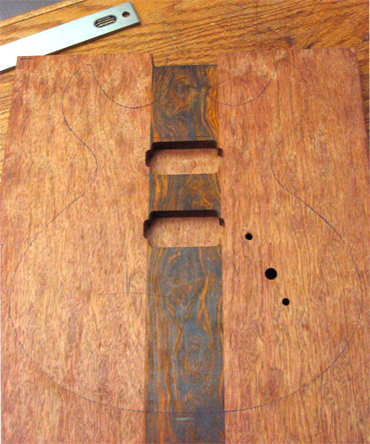 The guitar body blank with pickup cavities, electronics mouting holes and the outline of the guitar traced on the face